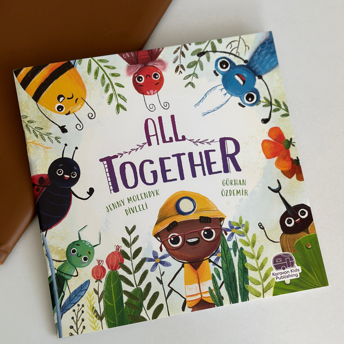 Children's book titled 'All Together' with colorful illustrations of insects and a child on a white surface.
