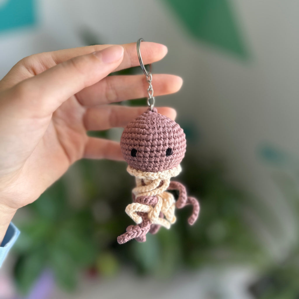 Hand holding a small crochet octopus keychain with a blurred green plant background