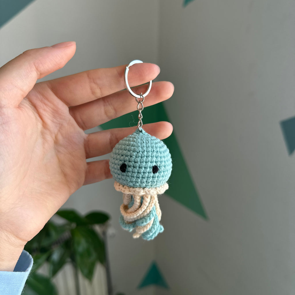 Hand holding a small blue and beige crocheted keychain against a light background