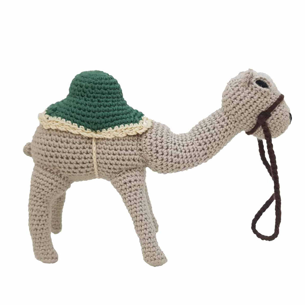 alt="Handmade beige crochet camel standing with green saddle and brown leash attached to the nose